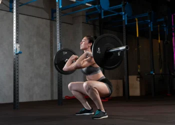 Pessoa realizando um exercício de thruster com barra para fortalecimento do ombro, glúteos e queima de gordura.