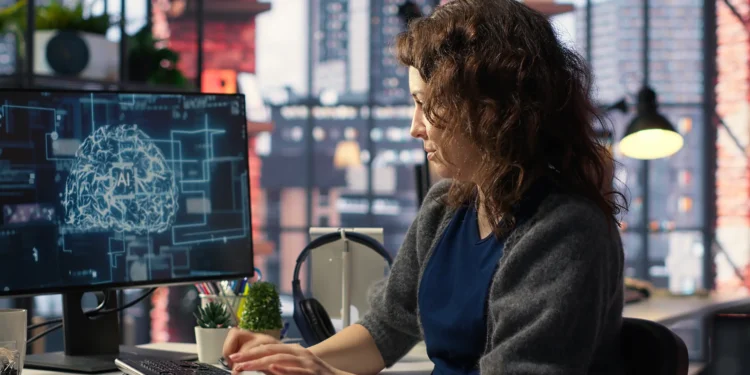 Pesquisadora trabalhando em frente a um monitor com visualização de IA, ilustrando estudo sobre estereótipos femininos em plataformas de inteligência artificial.